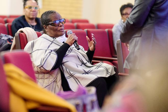Photo Of Yvonne Hughes seated and holding a microphone